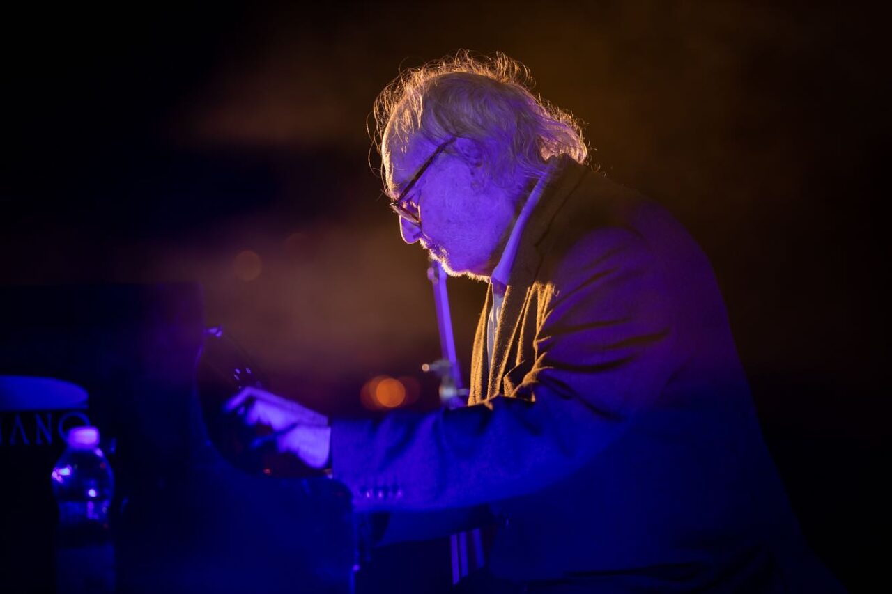 Foto de un pianista de perfil tocando de noche en un escenario